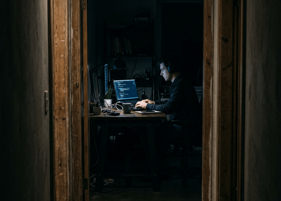 Person wearing headphones working on coding at a laptop in a dark room