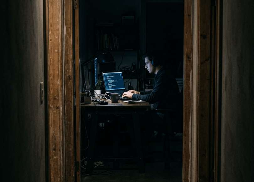 Person wearing headphones working on coding at a laptop in a dark room