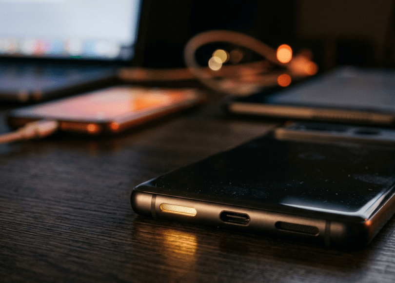 Several smartphones and a laptop placed on a dark wooden desk under low light
