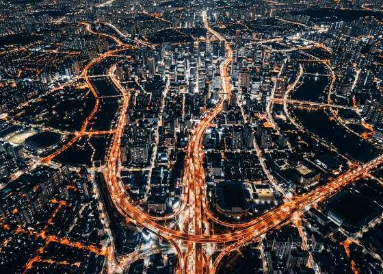 Aerial nighttime cityscape showing illuminated highways and buildings with flowing traffic lights.