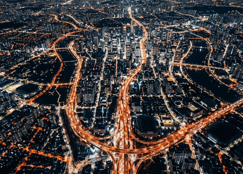Aerial nighttime cityscape showing illuminated highways and buildings with flowing traffic lights.