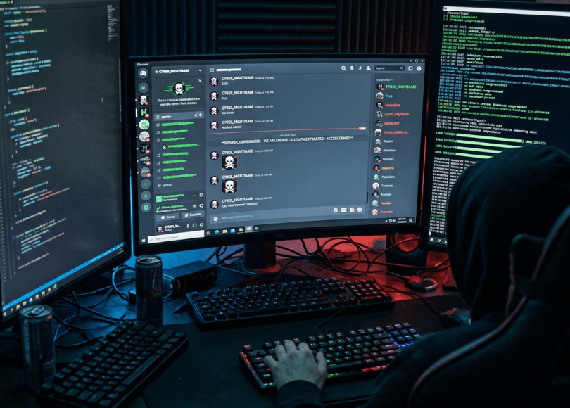 Person at computer with multiple screens displaying code and chat messages.